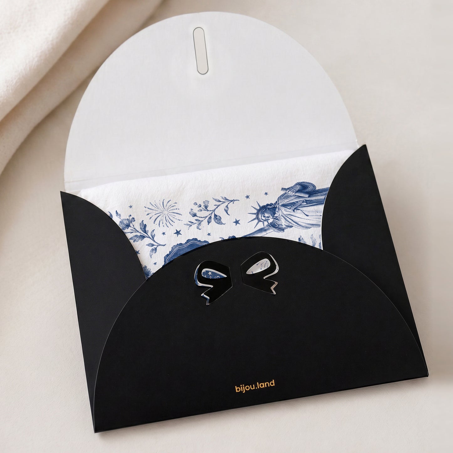 Navy toile America 250th anniversary tea towel tucked inside a black gift envelope with a bow, showing the gift-ready packaging option