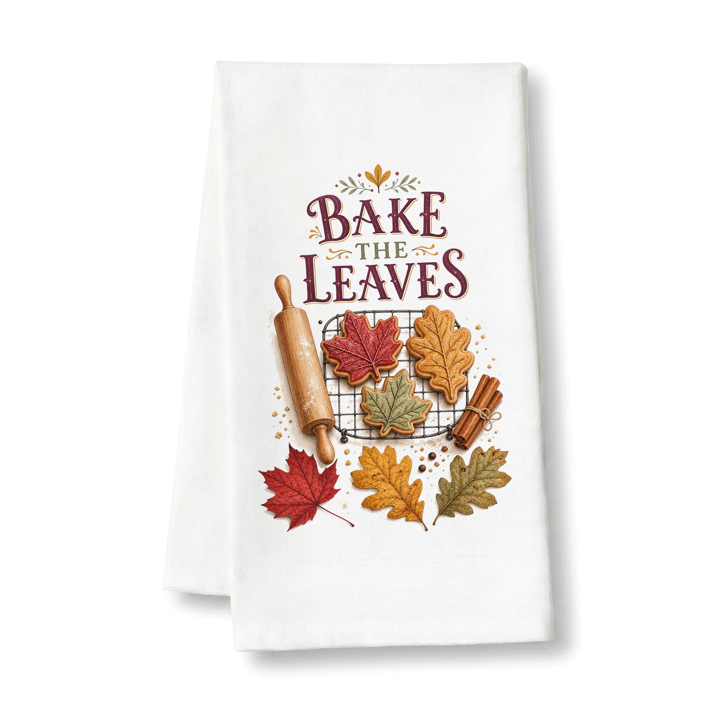 Bake the Leaves Fall Baking Tea Towel folded on a clean white background, showing leaf-shaped cookies, cooling rack, rolling pin, cinnamon, and autumn leaves.