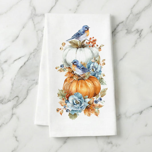 Bluebird Pumpkin autumn tea towel folded on white marble, with the full bluebird, pumpkin, and floral print visible.