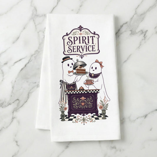 Spirit Service Ghost Halloween Kitchen Towel folded on white marble, with two friendly ghosts serving cake and tea at a vintage cafe counter clearly shown.