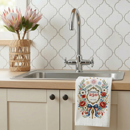 America 250 botanical wreath tea towel displayed by a kitchen sink, showing floral patriotic artwork on a white towel
