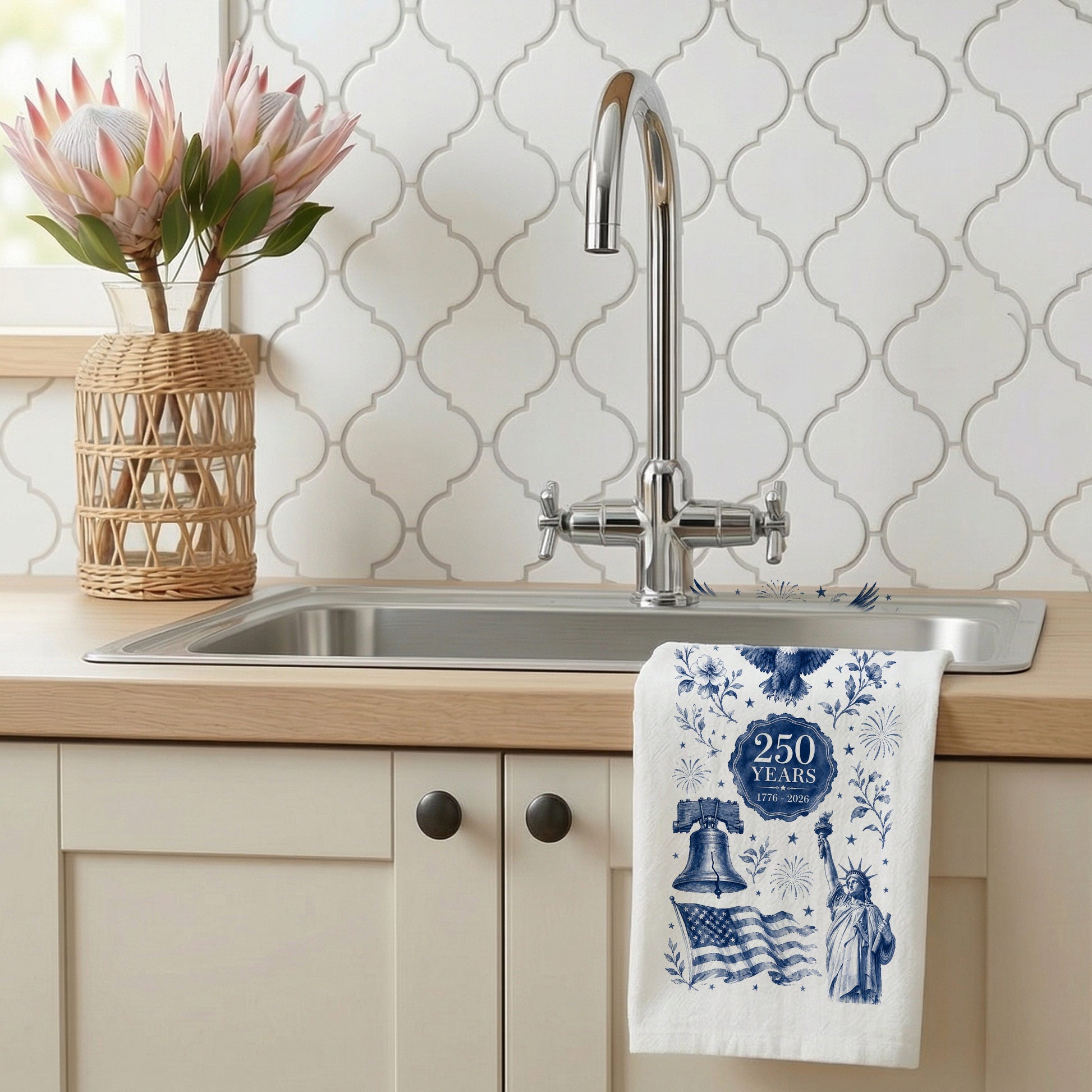 Navy toile America 250th anniversary tea towel hanging at a kitchen sink beside flowers and patterned tile