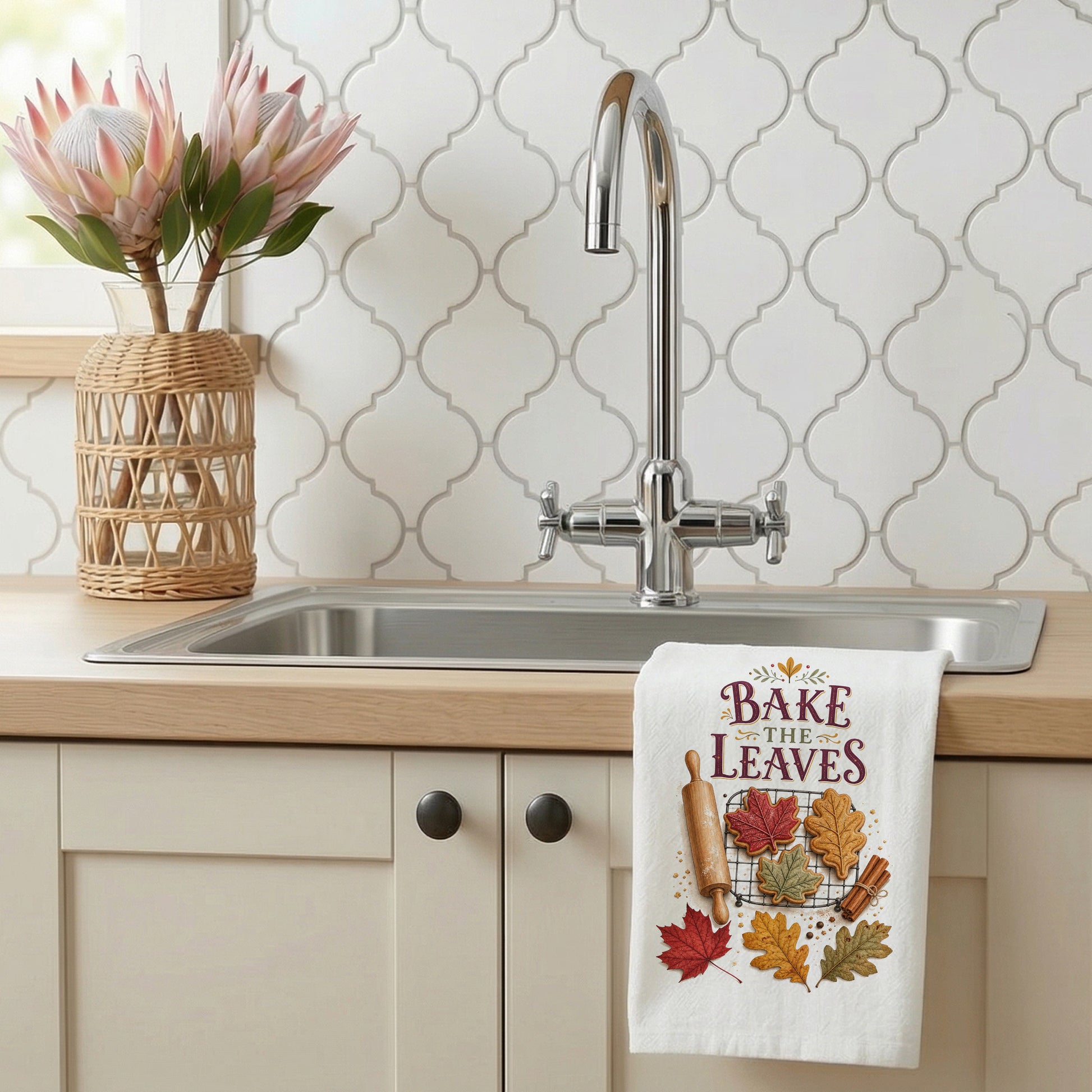 Bake the Leaves Fall Baking Tea Towel styled beside a bright kitchen sink, with leaf-shaped cookies, cooling rack, rolling pin, cinnamon, and autumn leaves shown.