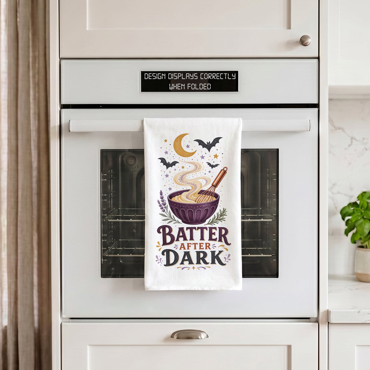 Batter After Dark Halloween Kitchen Towel draped over an oven handle, with the artwork centered when folded.