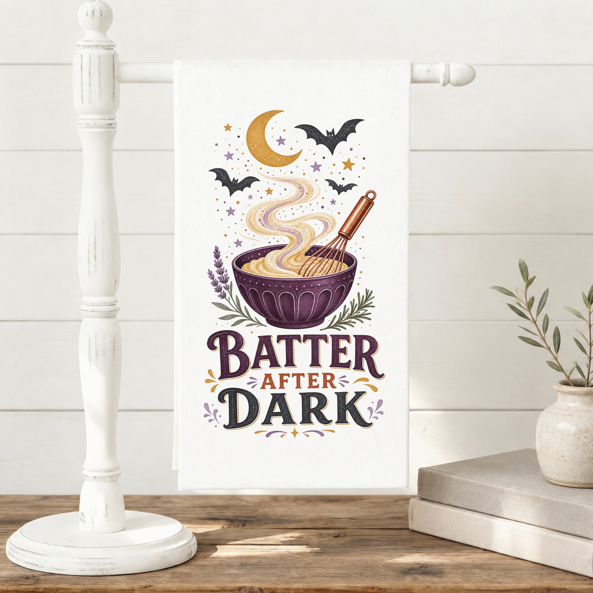 Batter After Dark Halloween Kitchen Towel displayed on a freestanding towel stand, with whisk, mixing bowl, curling batter, crescent moon, stars, and bats clearly shown.
