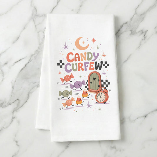 Candy Curfew Retro Halloween Kitchen Towel folded on white marble, with cheerful pastel candies, candy corn, small door, clock, moon, and checkerboard accents clearly shown.