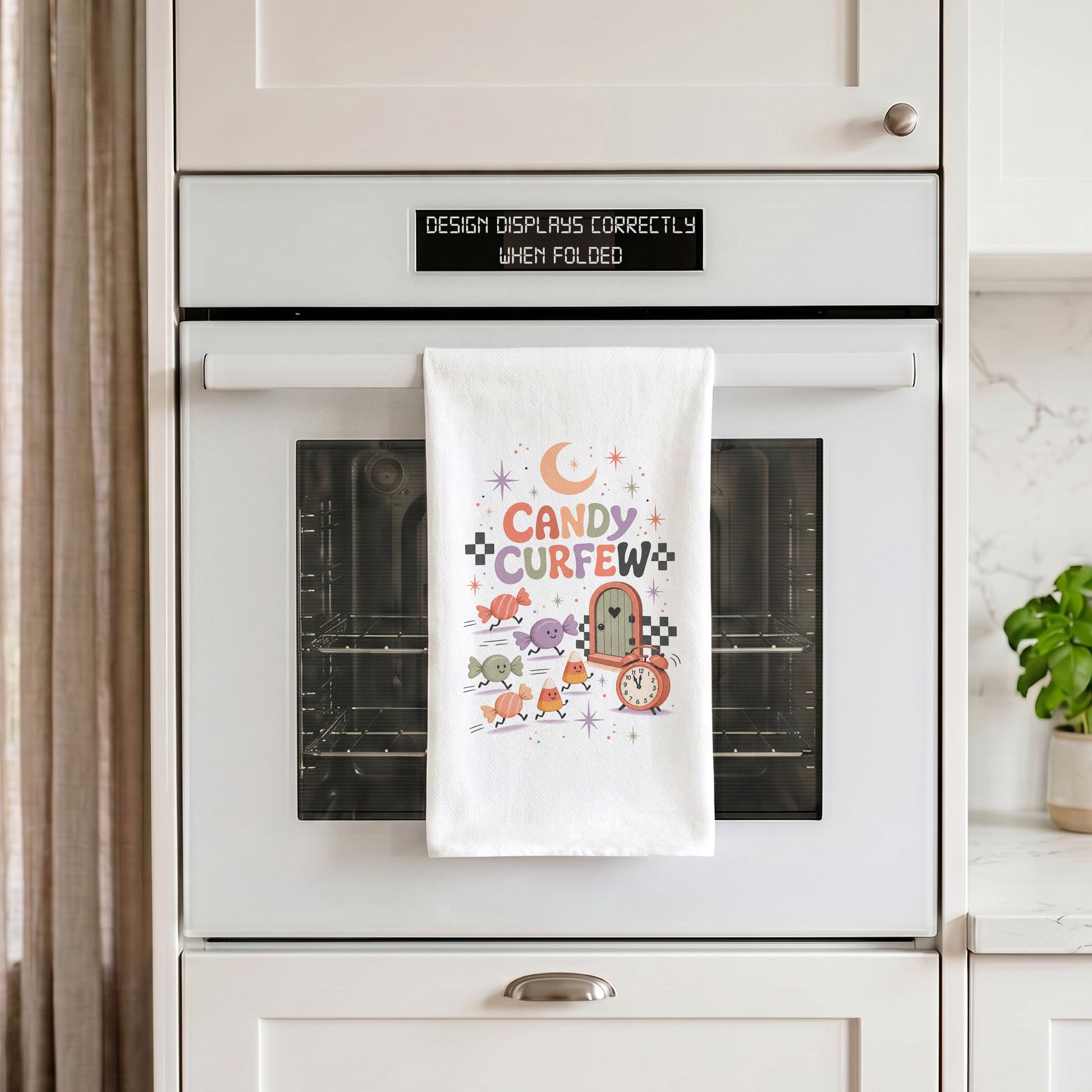 Candy Curfew Retro Halloween Kitchen Towel draped over an oven handle, with the artwork centered when folded.