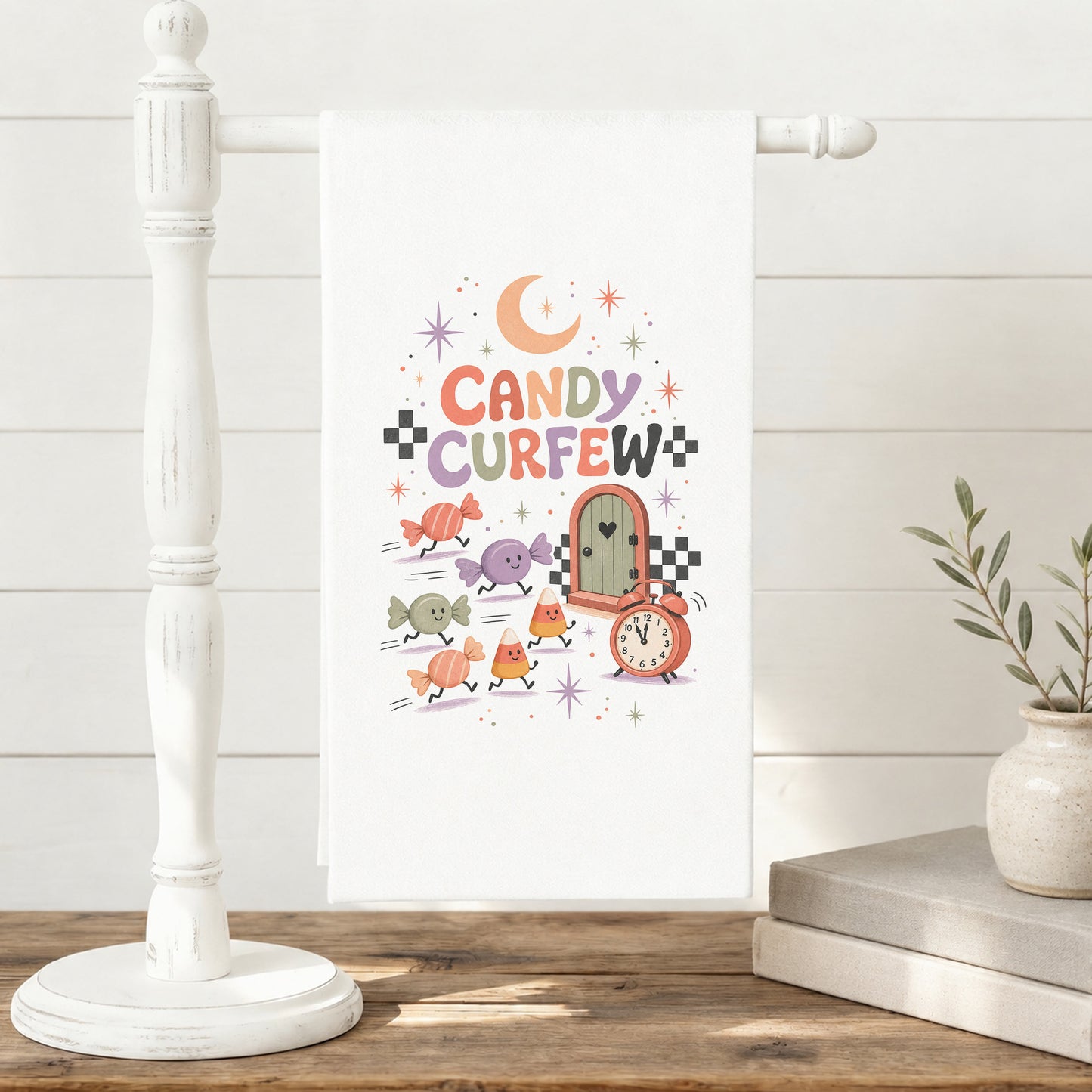 Candy Curfew Retro Halloween Kitchen Towel displayed on a freestanding towel stand, with cheerful pastel candies, candy corn, small door, clock, moon, and checkerboard accents clearly shown.