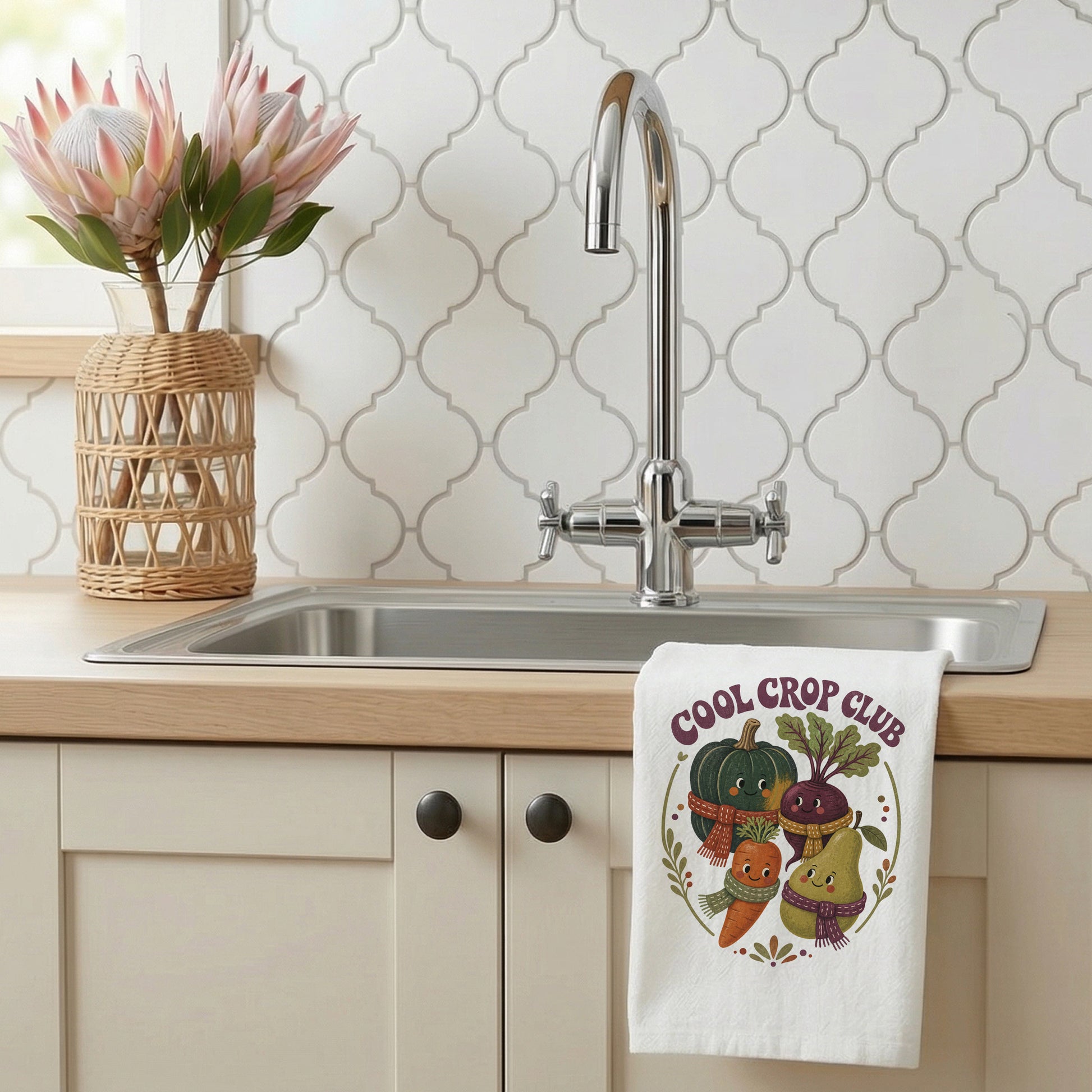 Cool Crop Club Harvest Tea Towel styled beside a bright kitchen sink, with smiling squash, beet, carrot, and pear characters wearing scarves shown.