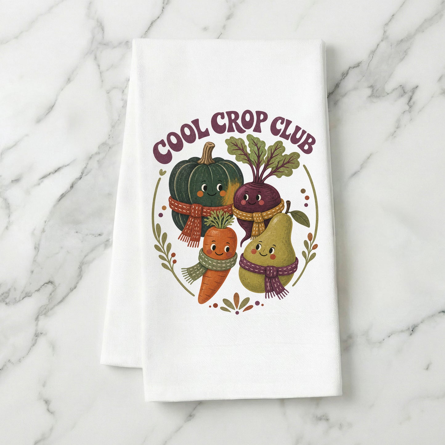Cool Crop Club Harvest Tea Towel folded on white marble, with smiling squash, beet, carrot, and pear characters wearing scarves clearly shown.
