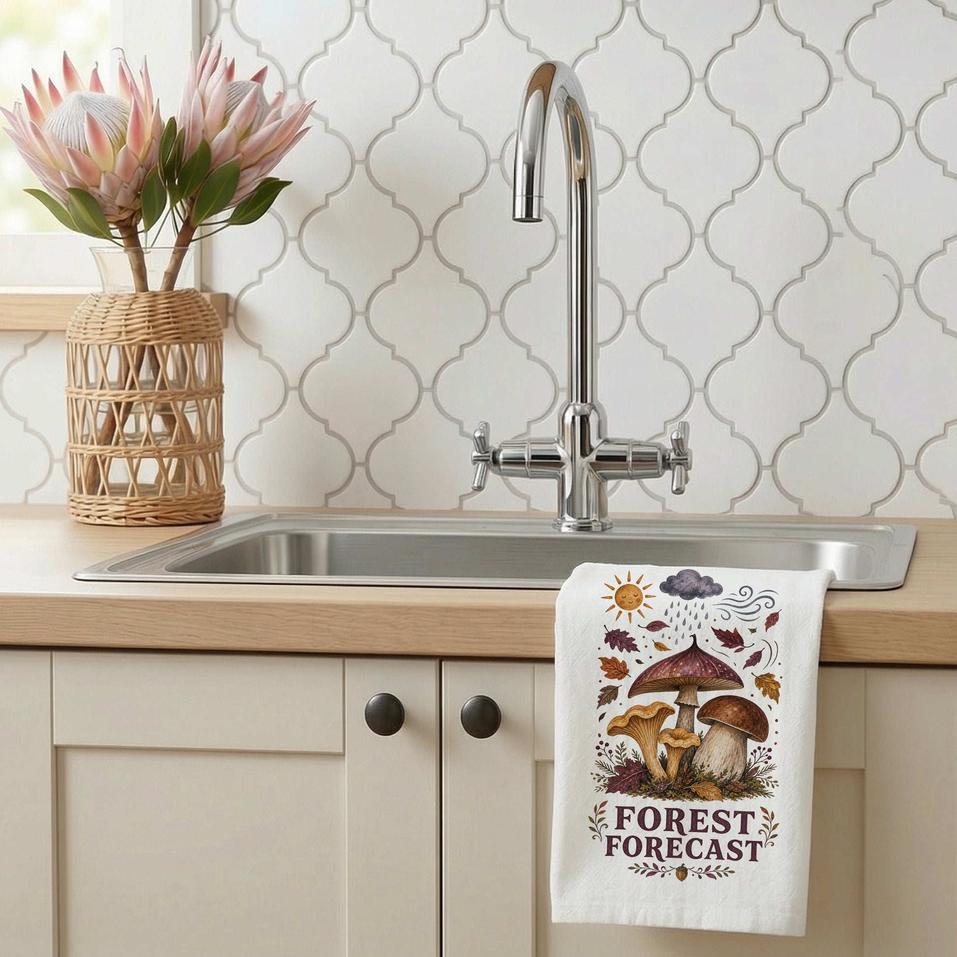 Forest Forecast Mushroom Tea Towel styled beside a bright kitchen sink, with woodland mushrooms, autumn leaves, sun, rain cloud, wind, and burgundy lettering shown.