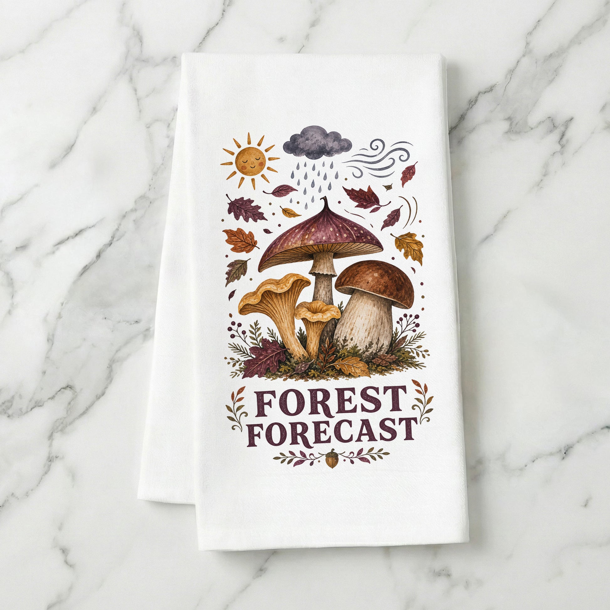 Forest Forecast Mushroom Tea Towel folded on white marble, with woodland mushrooms, autumn leaves, sun, rain cloud, wind, and burgundy lettering clearly shown.