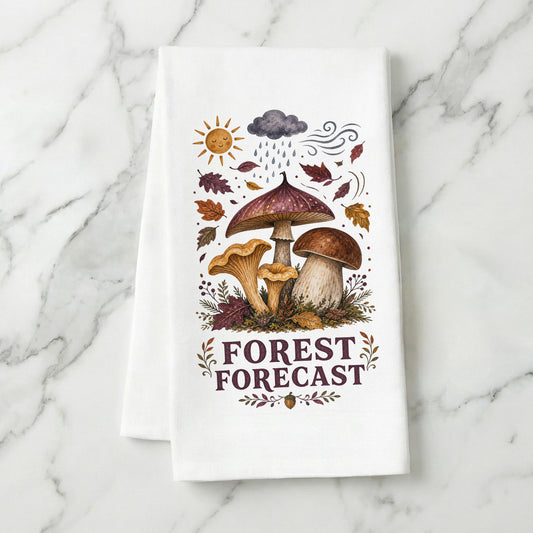 Forest Forecast Mushroom Tea Towel folded on white marble, with woodland mushrooms, autumn leaves, sun, rain cloud, wind, and burgundy lettering clearly shown.
