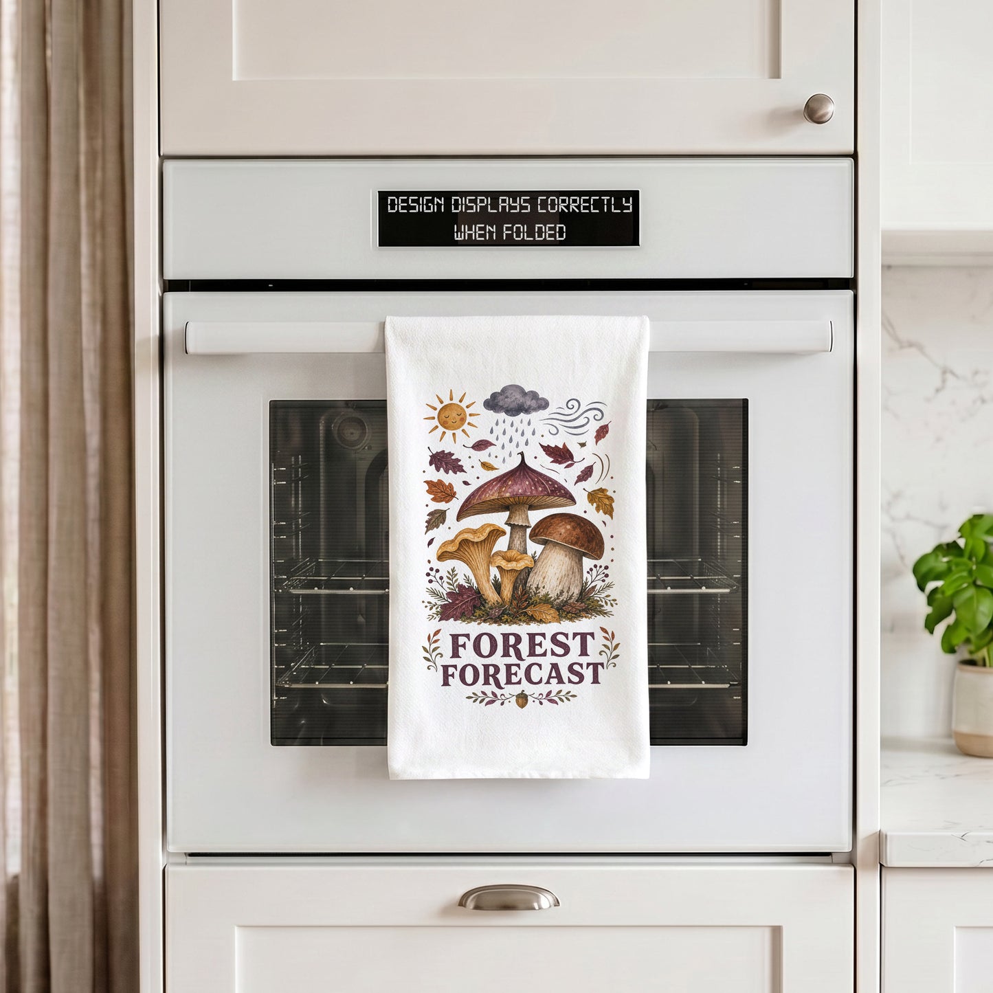 Forest Forecast Mushroom Tea Towel draped over an oven handle, with the artwork centered when folded.