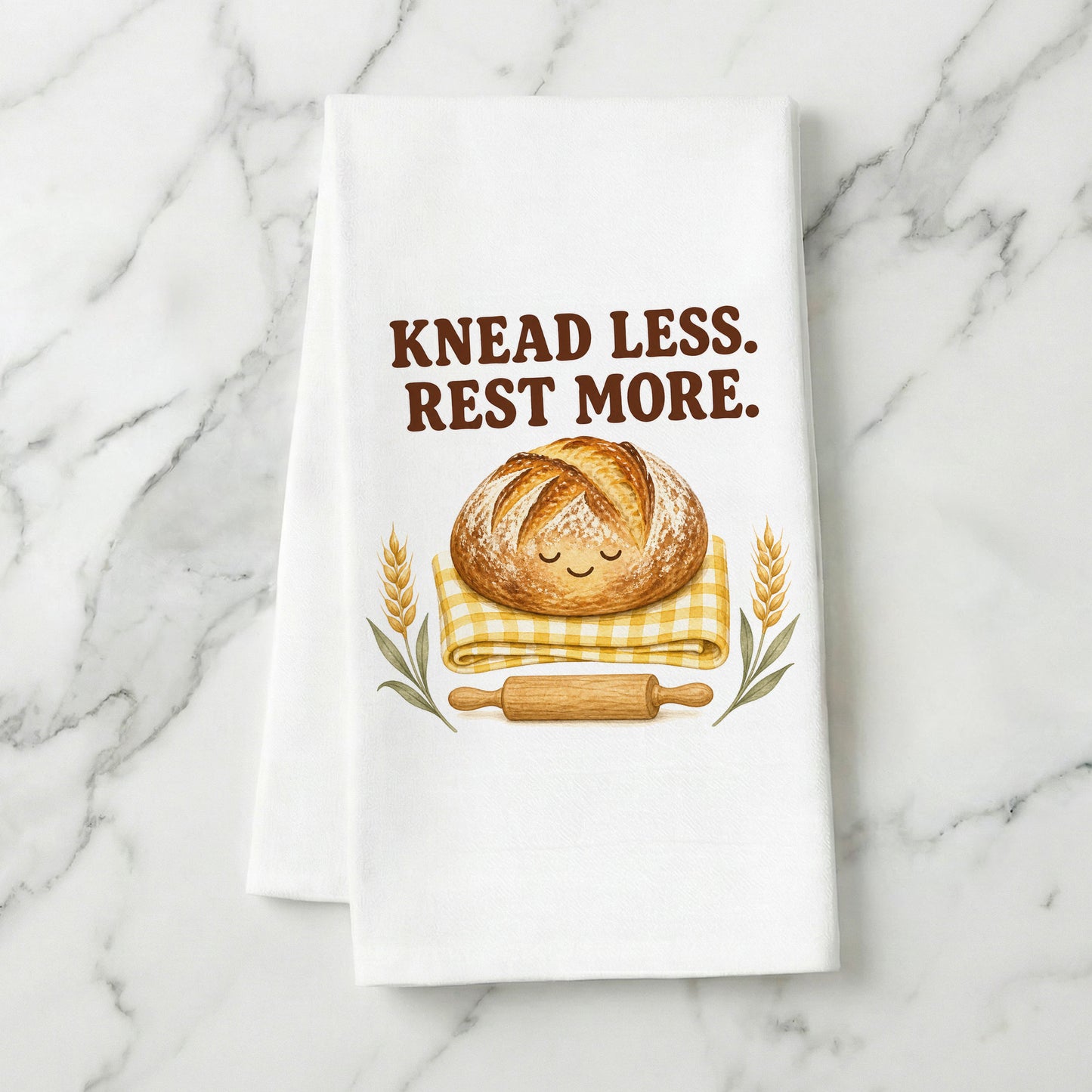 Knead Less Rest More sourdough tea towel styled on a marble surface.