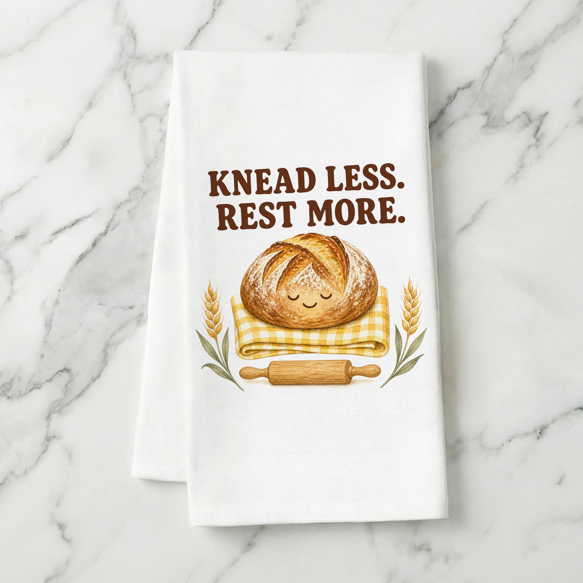Knead Less Rest More sourdough tea towel styled on a marble surface.
