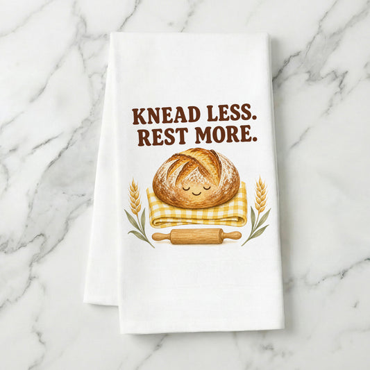 Knead Less Rest More sourdough tea towel styled on a marble surface.