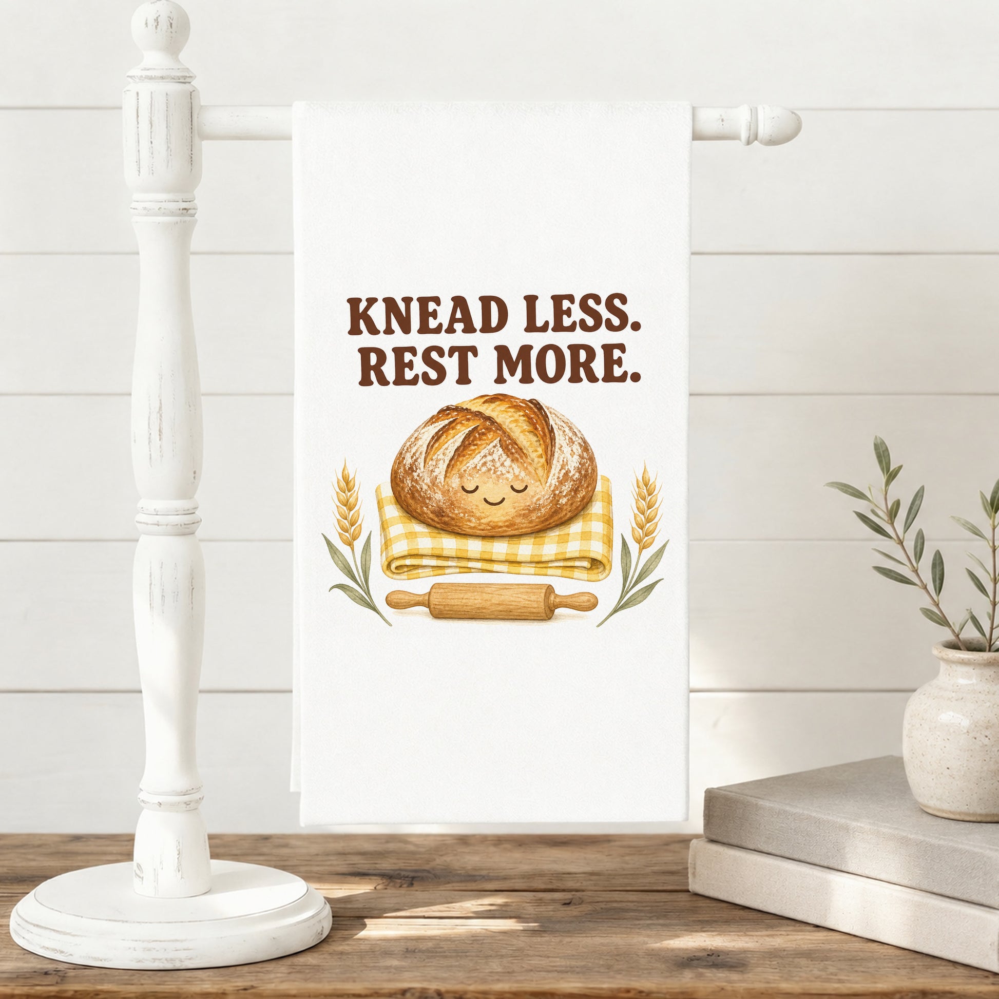 Knead Less Rest More sourdough tea towel displayed on a freestanding towel stand.