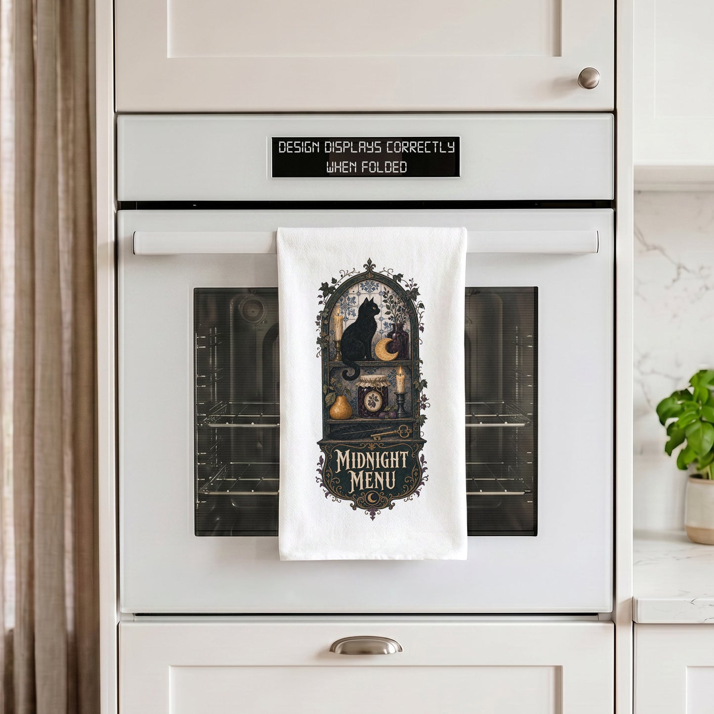 Midnight Menu Black Cat Halloween Kitchen Towel draped over an oven handle, with the artwork centered when folded.