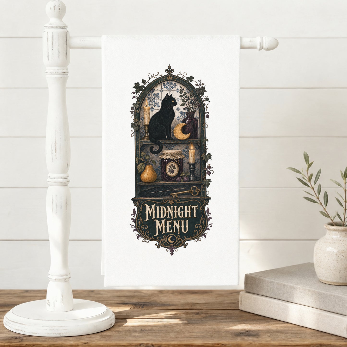 Midnight Menu Black Cat Halloween Kitchen Towel displayed on a freestanding towel stand, with black cat, candlelit pantry, moon cookie, pear, preserves, and antique details clearly shown.