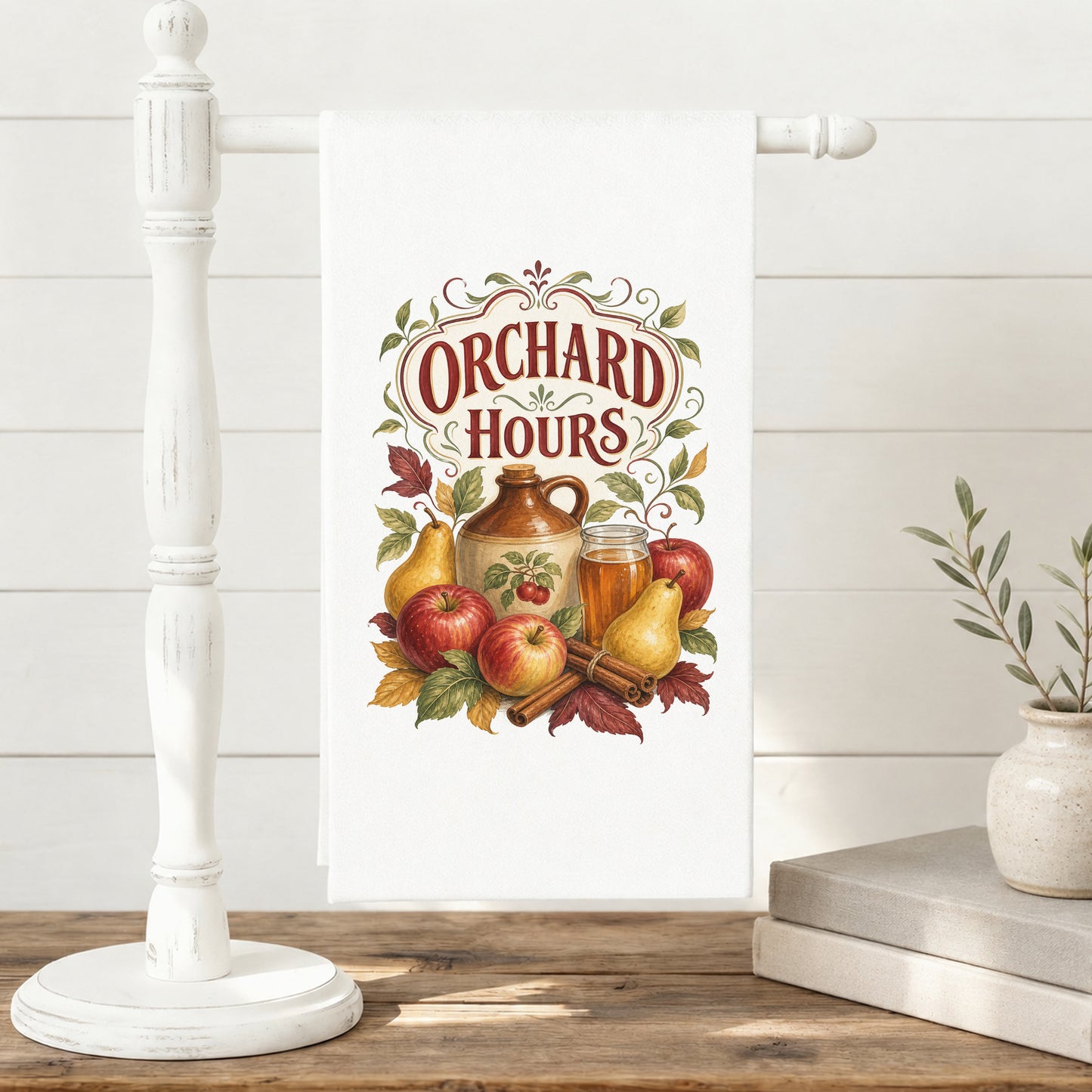 Orchard Hours Apple Cider Tea Towel displayed on a freestanding towel stand, with apples, pears, cider jug and glass, cinnamon sticks, leaves, and vintage lettering clearly shown.