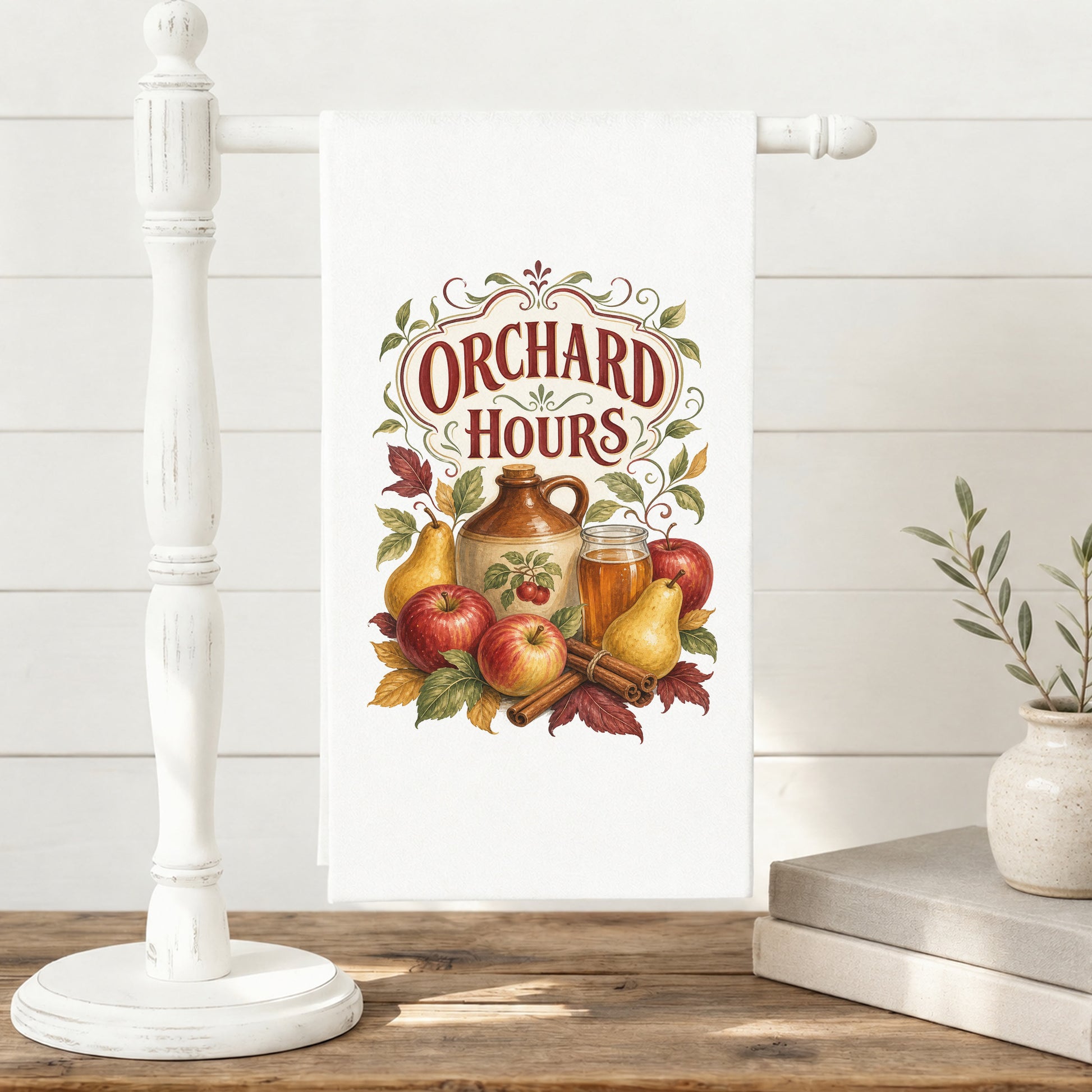 Orchard Hours Apple Cider Tea Towel displayed on a freestanding towel stand, with apples, pears, cider jug and glass, cinnamon sticks, leaves, and vintage lettering clearly shown.