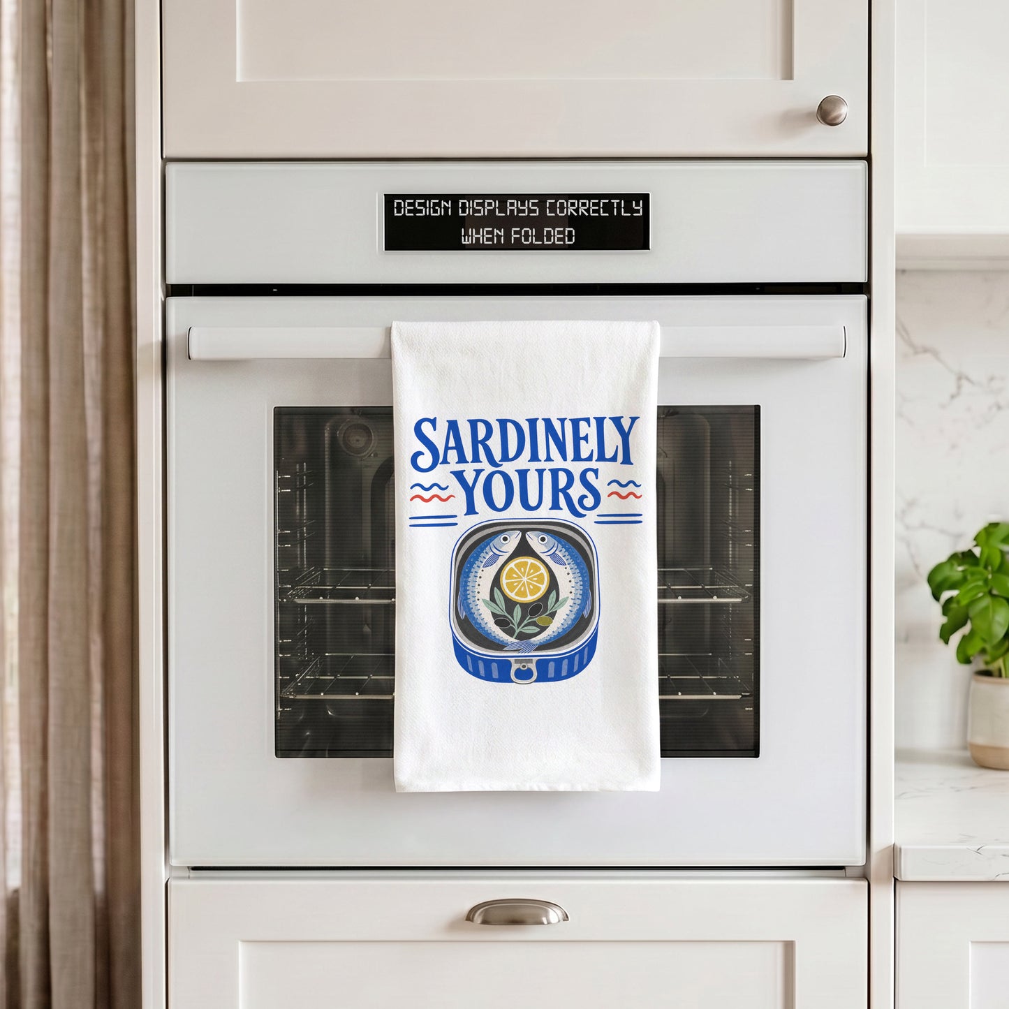 White Sardinely Yours tea towel draped over an oven handle in a kitchen setting.
