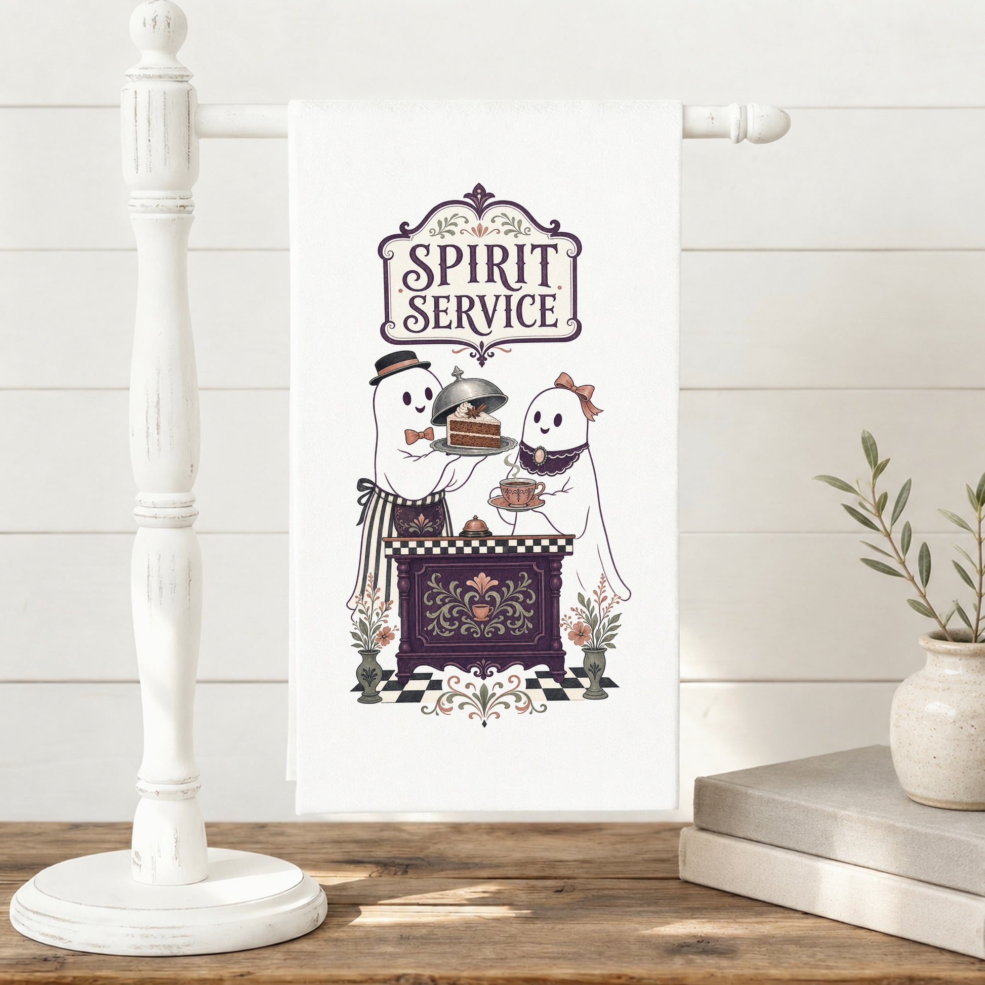 Spirit Service Ghost Halloween Kitchen Towel displayed on a freestanding towel stand, with two friendly ghosts serving cake and tea at a vintage cafe counter clearly shown.