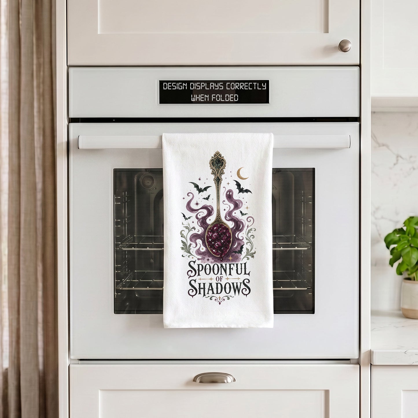 Spoonful of Shadows Gothic Halloween Kitchen Towel draped over an oven handle, with the artwork centered when folded.