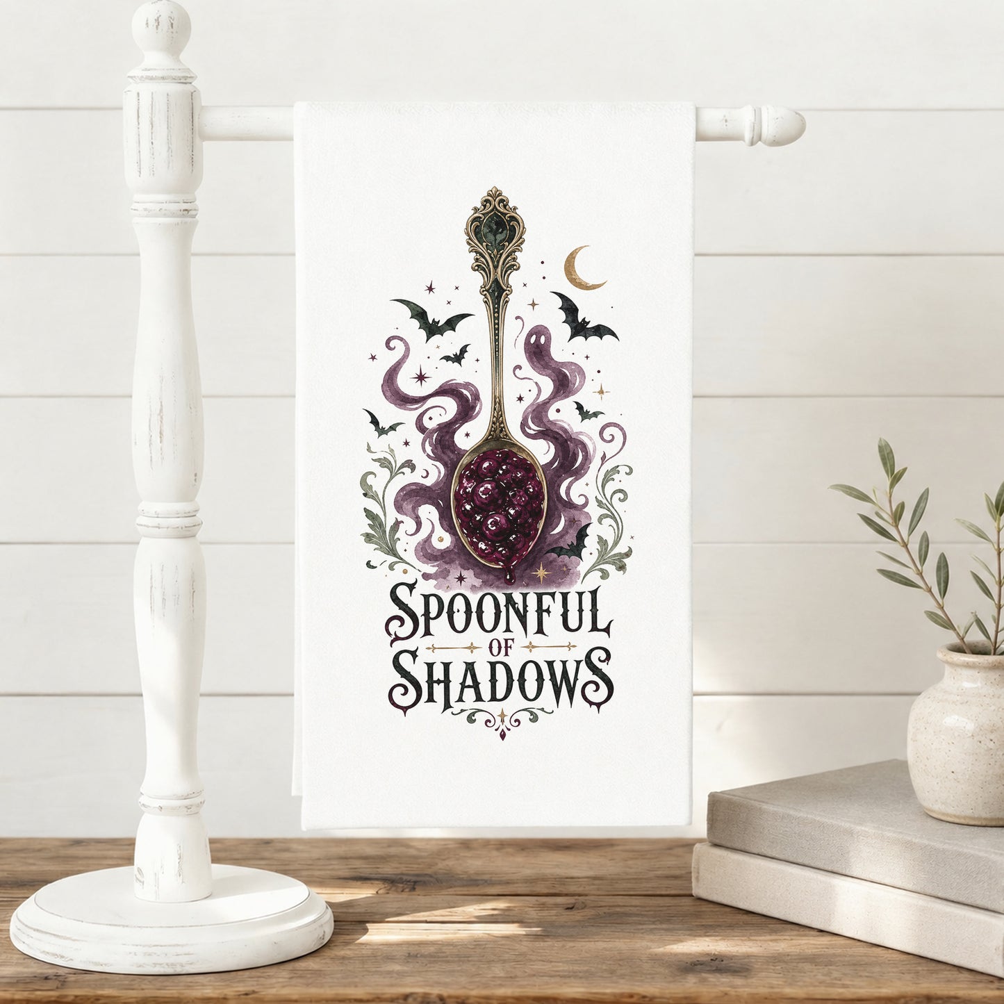Spoonful of Shadows Gothic Halloween Kitchen Towel displayed on a freestanding towel stand, with ornate spoon, berry jam, curling ghost shapes, bats, and crescent moon clearly shown.