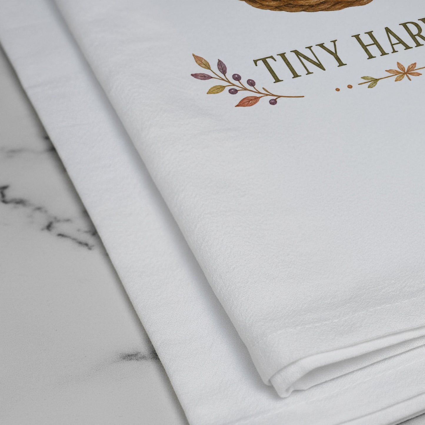Close-up of the Tiny Harvest Autumn Tea Towel print showing woven basket filled with pears, squash, mushrooms, chestnuts, herbs, and flowers on white flour sack organic cotton.