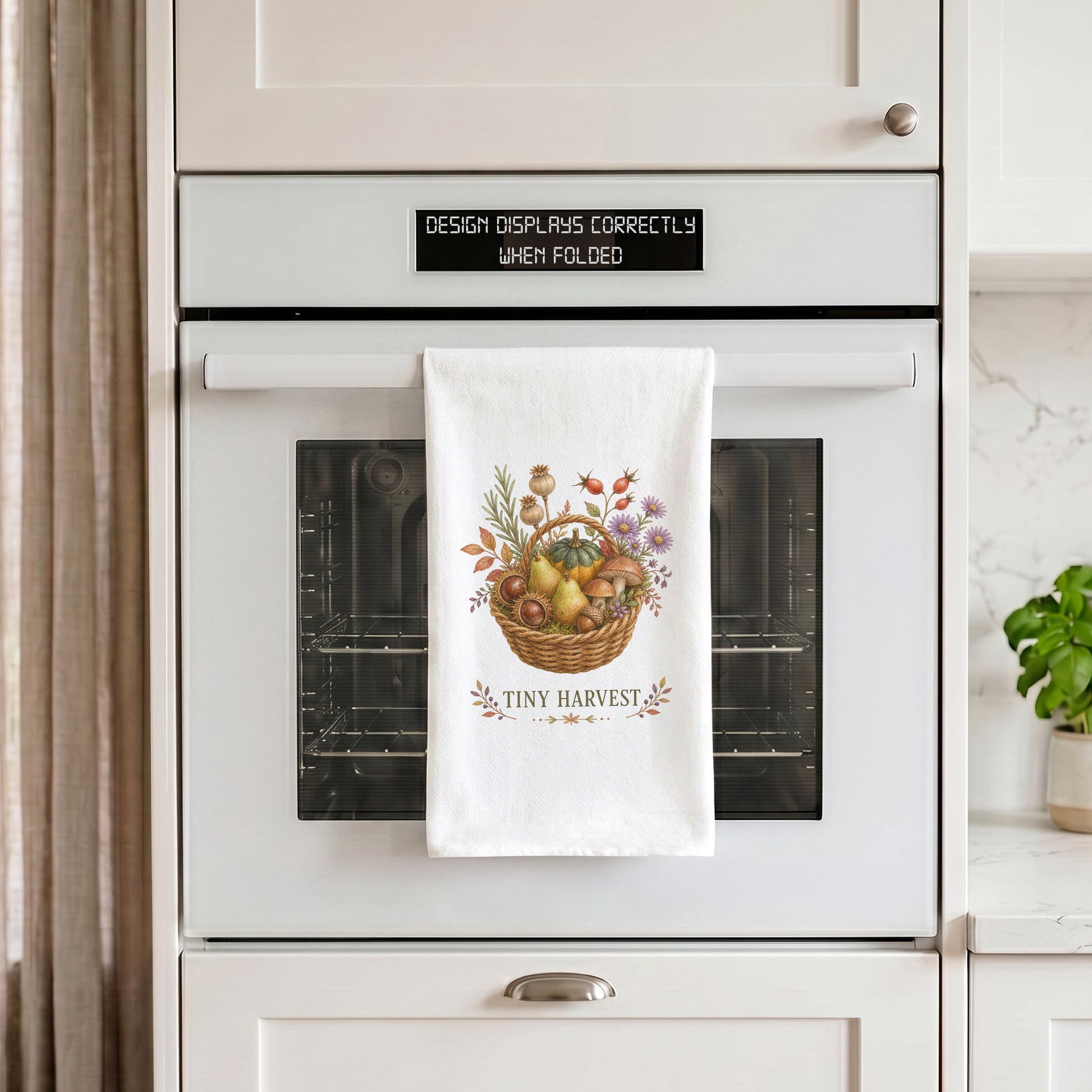 Tiny Harvest Autumn Tea Towel draped over an oven handle, with the artwork centered when folded.