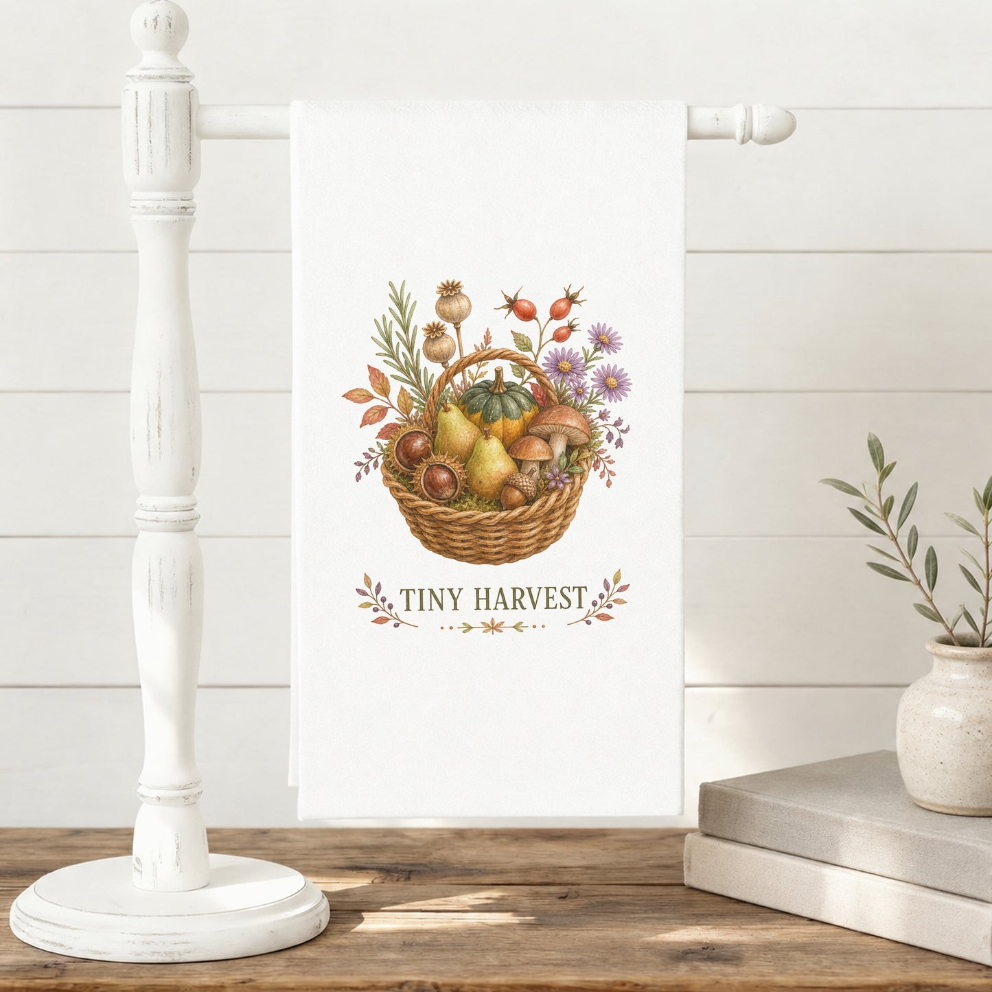 Tiny Harvest Autumn Tea Towel displayed on a freestanding towel stand, with woven basket filled with pears, squash, mushrooms, chestnuts, herbs, and flowers clearly shown.