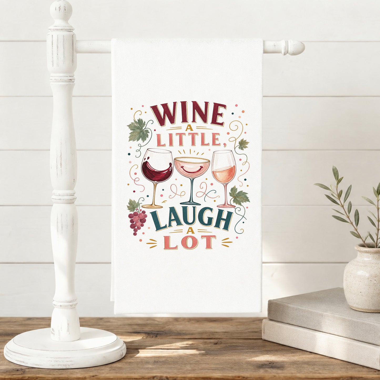 Wine a Little, Laugh a Lot tea towel displayed on a freestanding towel stand.